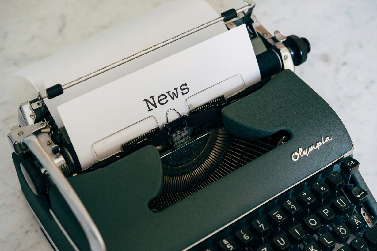 Schwarze Olympia-Schreibmaschine mit eingespannter Seite und dem Wort „News“ im Schriftbild.